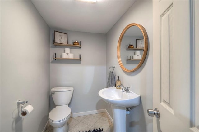 half bath featuring baseboards, a sink, toilet, and tile patterned floors