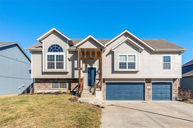 bi-level home featuring a garage, a front yard, stone siding, and concrete driveway