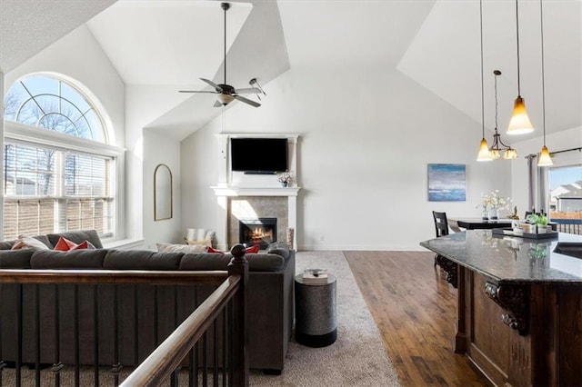 living room with dark wood-style floors, ceiling fan, a lit fireplace, and high vaulted ceiling