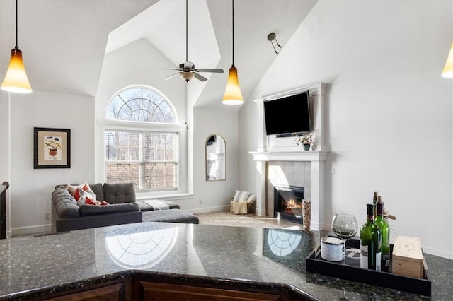 living area with high vaulted ceiling, a tile fireplace, a ceiling fan, and baseboards