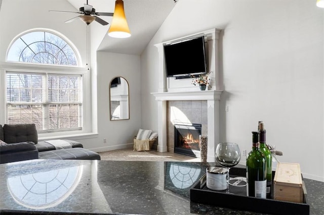 living room featuring a ceiling fan, lofted ceiling, baseboards, and a tiled fireplace