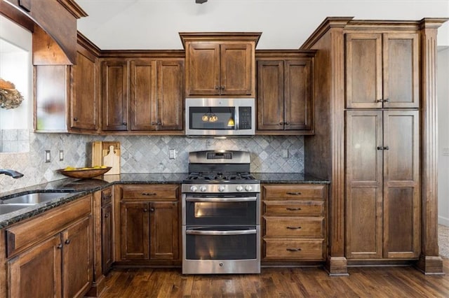 kitchen featuring dark wood-type flooring, a sink, appliances with stainless steel finishes, dark stone counters, and tasteful backsplash