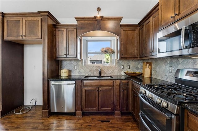 kitchen with dark wood-type flooring, dark stone countertops, stainless steel appliances, and a sink