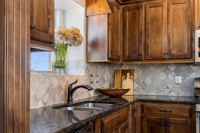 kitchen featuring stainless steel microwave, backsplash, dark stone counters, and a sink