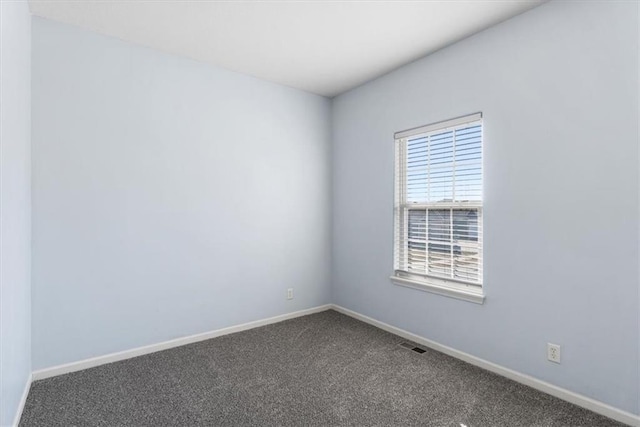 spare room with dark colored carpet, visible vents, and baseboards