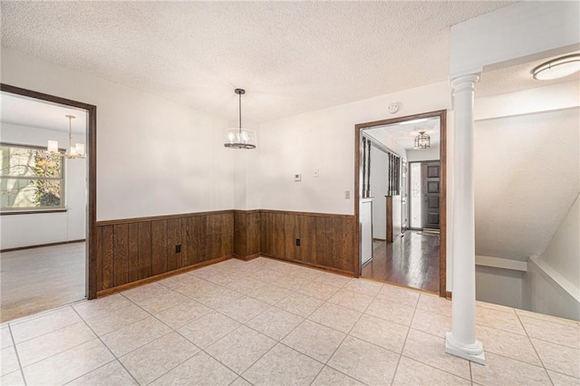 spare room with wooden walls, wainscoting, a textured ceiling, and an inviting chandelier