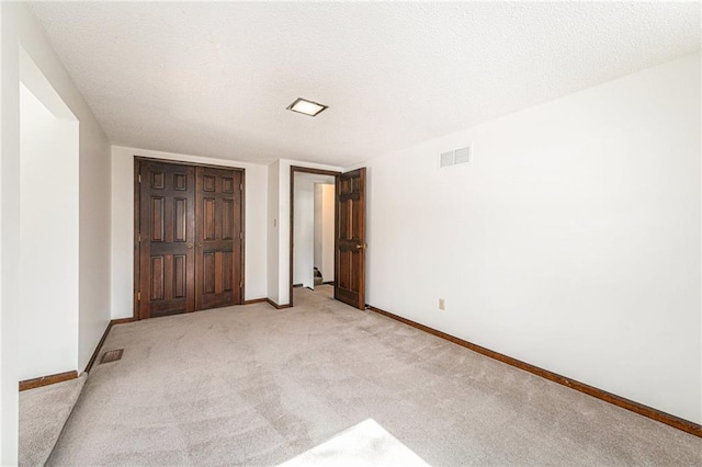 unfurnished bedroom featuring baseboards, light colored carpet, visible vents, and a textured ceiling