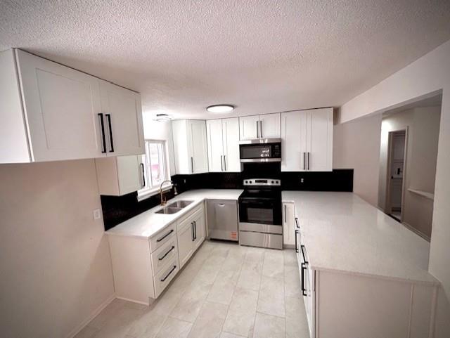 kitchen featuring stainless steel appliances, light countertops, a sink, and a peninsula