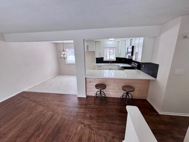 kitchen with a peninsula, stove, wood finished floors, a sink, and a kitchen breakfast bar