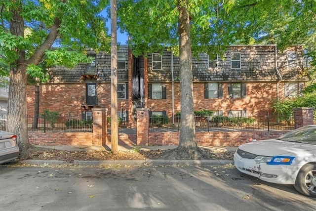 townhome / multi-family property featuring brick siding, fence, and mansard roof