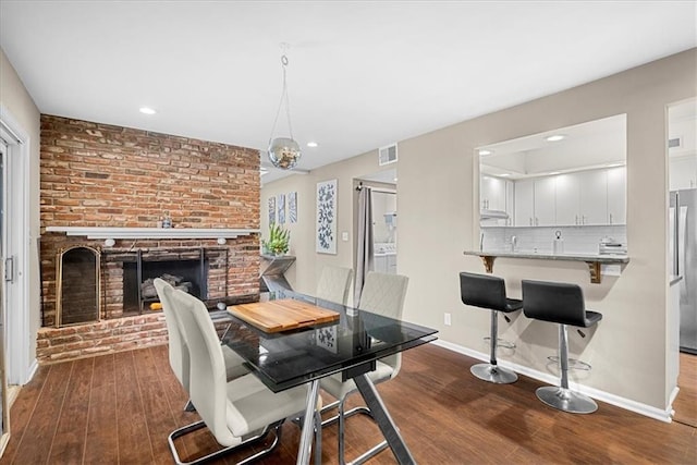 dining space with a brick fireplace, baseboards, visible vents, and hardwood / wood-style floors