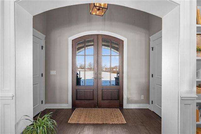 foyer entrance featuring arched walkways, a water view, baseboards, french doors, and dark wood finished floors