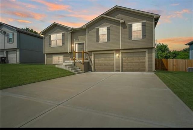 raised ranch featuring a garage, driveway, a front lawn, and fence