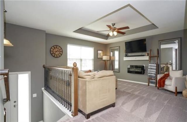 carpeted living room with a glass covered fireplace, a raised ceiling, ceiling fan, and baseboards