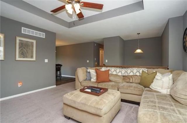 carpeted living room with a ceiling fan, a raised ceiling, visible vents, and baseboards