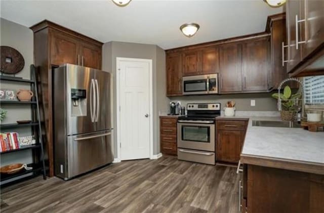 kitchen featuring dark brown cabinetry, appliances with stainless steel finishes, light countertops, and dark wood-style flooring