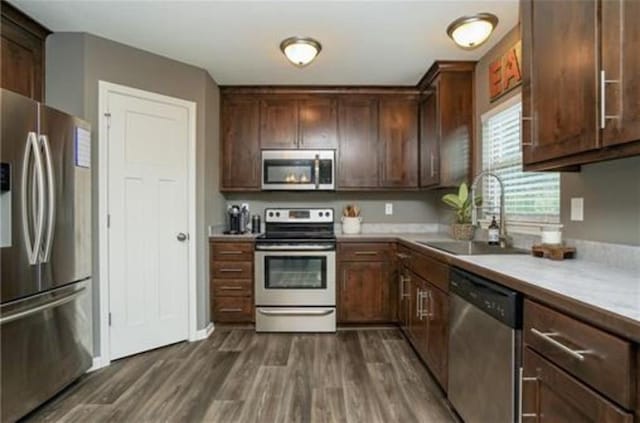 kitchen with dark wood finished floors, light countertops, appliances with stainless steel finishes, a sink, and dark brown cabinetry