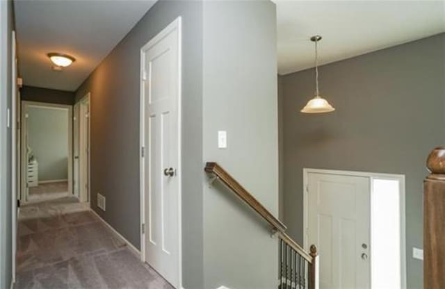 corridor featuring baseboards, dark carpet, visible vents, and an upstairs landing