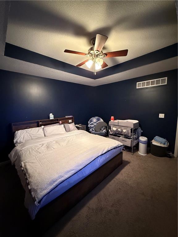 bedroom with a textured ceiling, visible vents, a raised ceiling, and carpet flooring