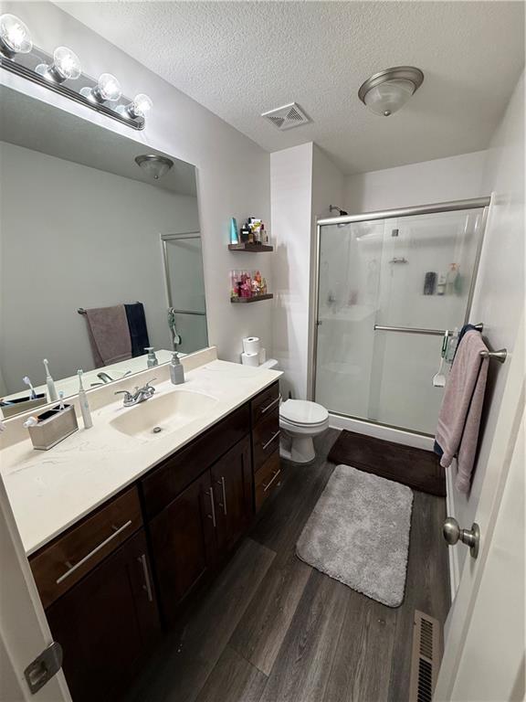 full bath featuring a textured ceiling, wood finished floors, visible vents, and a shower stall