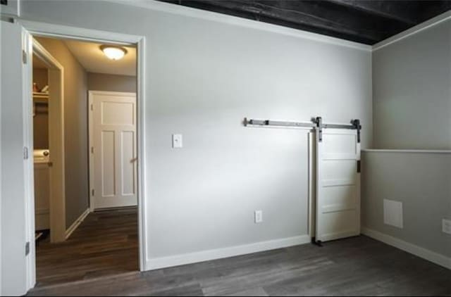 empty room featuring a barn door, baseboards, and dark wood-type flooring