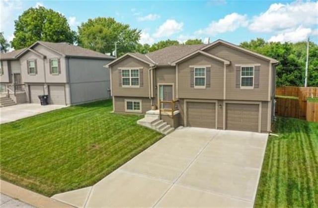 raised ranch featuring a garage, fence, a front lawn, and concrete driveway