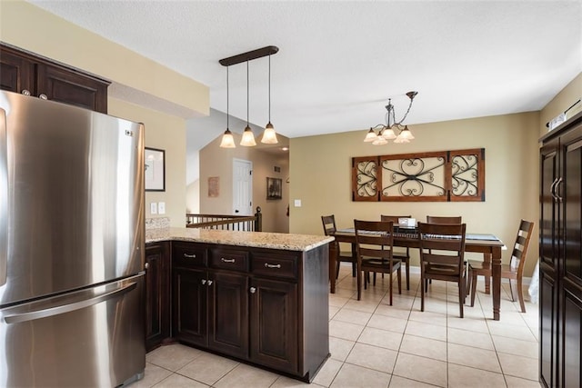 kitchen with pendant lighting, light stone counters, freestanding refrigerator, a peninsula, and dark brown cabinets