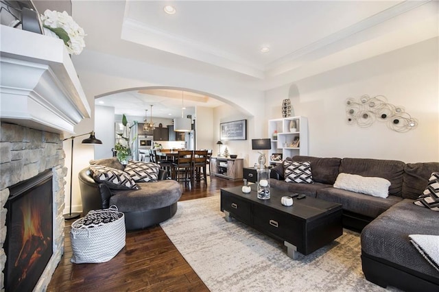 living room with arched walkways, a stone fireplace, recessed lighting, wood finished floors, and a raised ceiling