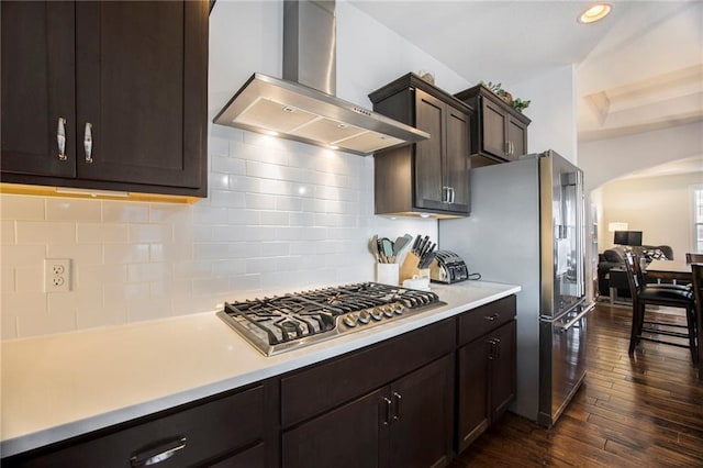 kitchen with stainless steel appliances, dark wood-type flooring, light countertops, wall chimney exhaust hood, and tasteful backsplash