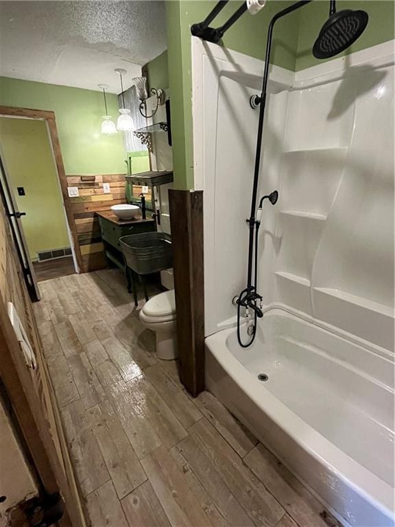 full bath featuring a textured ceiling, toilet, shower / bath combination, wood finished floors, and visible vents