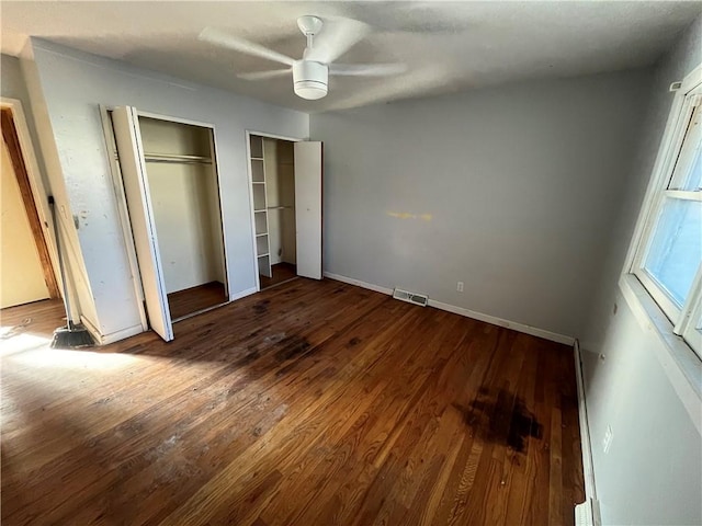 unfurnished bedroom with wood finished floors, visible vents, baseboards, a ceiling fan, and two closets