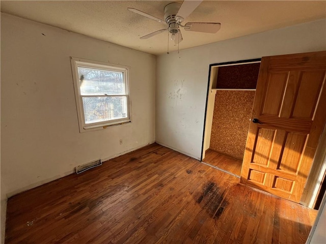 unfurnished bedroom with a closet, visible vents, a ceiling fan, a textured ceiling, and wood finished floors