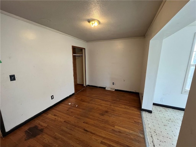 unfurnished room with baseboards, visible vents, wood finished floors, crown molding, and a textured ceiling