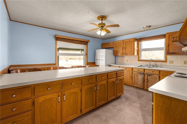 kitchen featuring light carpet, brown cabinets, freestanding refrigerator, and a sink