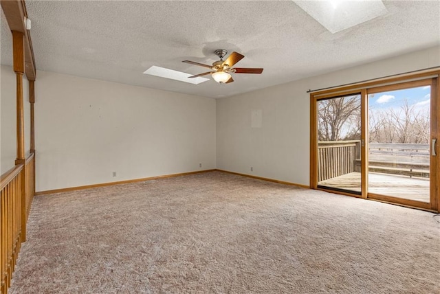 carpeted spare room with a skylight, baseboards, and ceiling fan