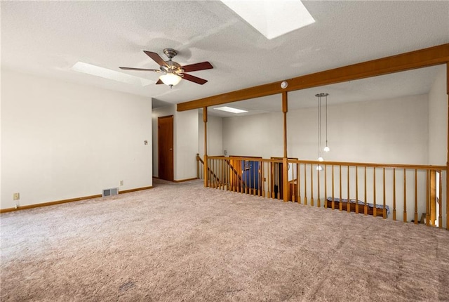 carpeted spare room with visible vents, ceiling fan, beam ceiling, a skylight, and a textured ceiling