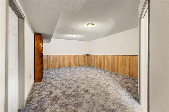 carpeted empty room featuring a textured ceiling, wooden walls, and wainscoting