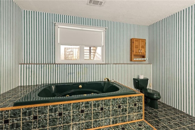 full bath with visible vents, a textured ceiling, toilet, and a tub with jets