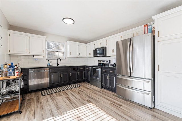 kitchen featuring appliances with stainless steel finishes, white cabinetry, a sink, and dark cabinets