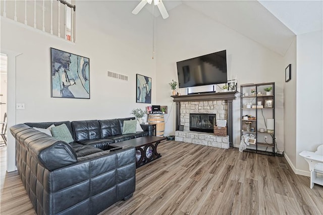 living area with visible vents, ceiling fan, wood finished floors, a fireplace, and high vaulted ceiling