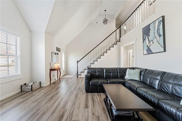 living area with high vaulted ceiling, stairs, baseboards, and wood finished floors