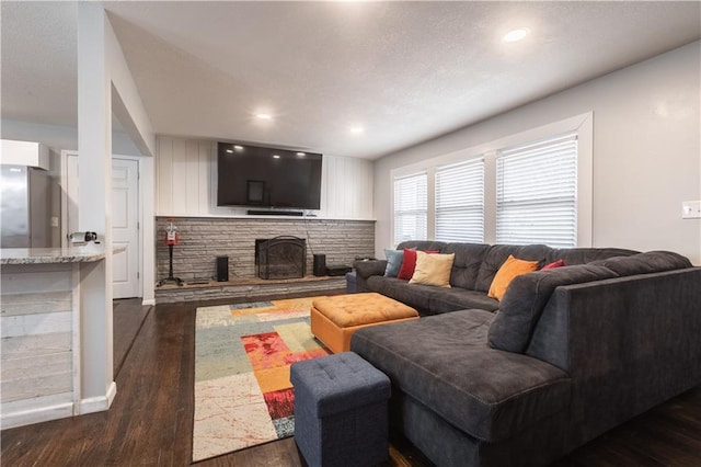 living area with dark wood-type flooring, recessed lighting, and a stone fireplace