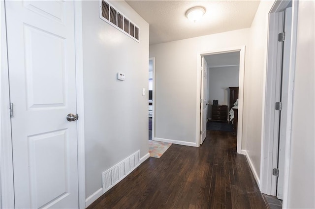 hallway with dark wood-style floors, visible vents, and baseboards