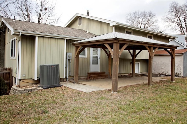 rear view of property featuring entry steps, a shingled roof, cooling unit, and a yard