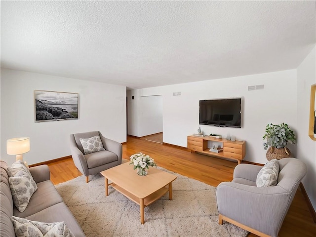 living area with baseboards, a textured ceiling, visible vents, and wood finished floors