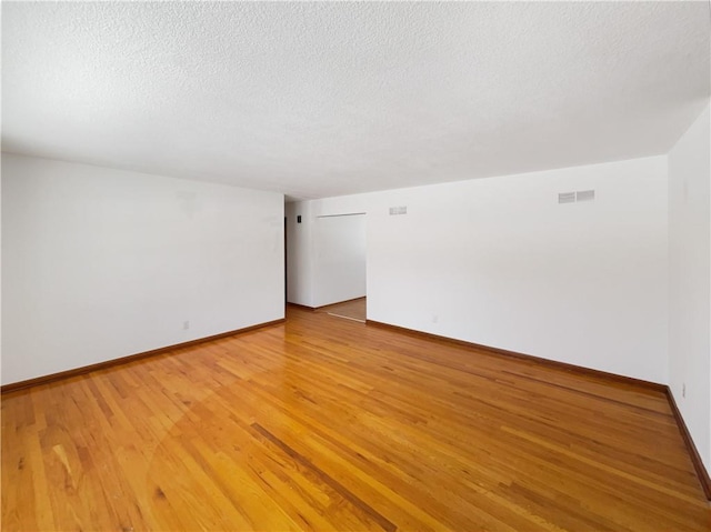 unfurnished room with a textured ceiling, light wood finished floors, visible vents, and baseboards