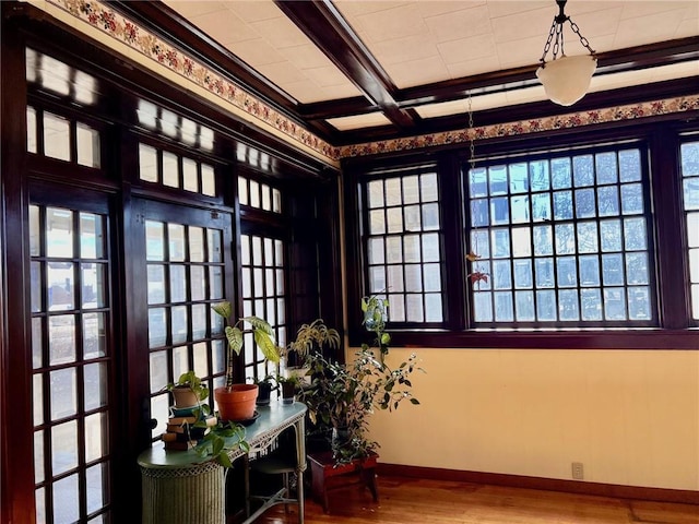 interior space with beam ceiling, coffered ceiling, baseboards, and wood finished floors