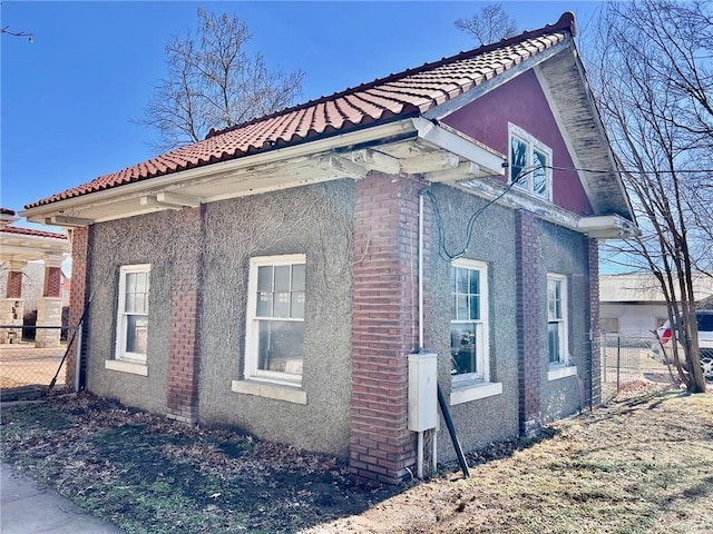 view of side of property featuring brick siding, a tile roof, fence, and stucco siding