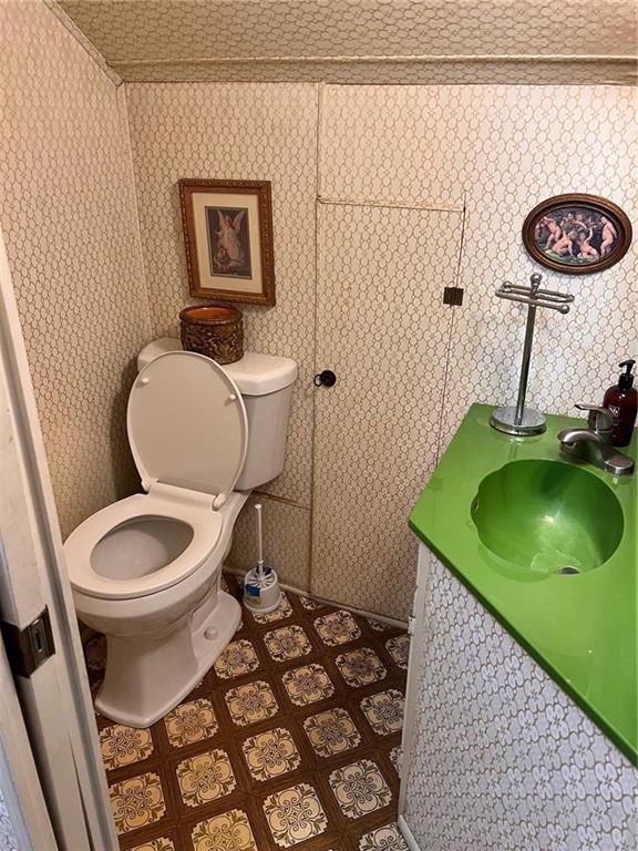 half bathroom featuring vanity, toilet, and wallpapered walls