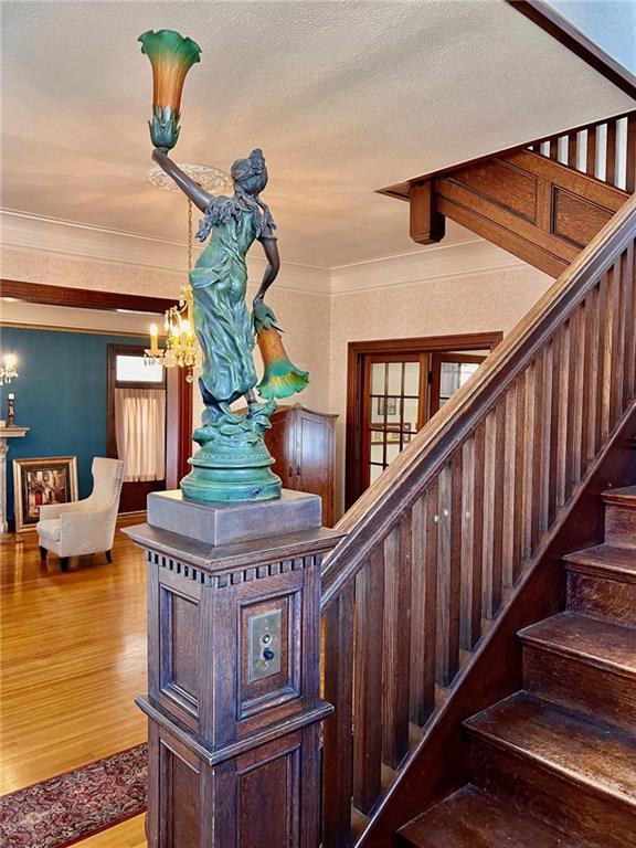 stairway with a textured ceiling, an inviting chandelier, wood finished floors, and crown molding